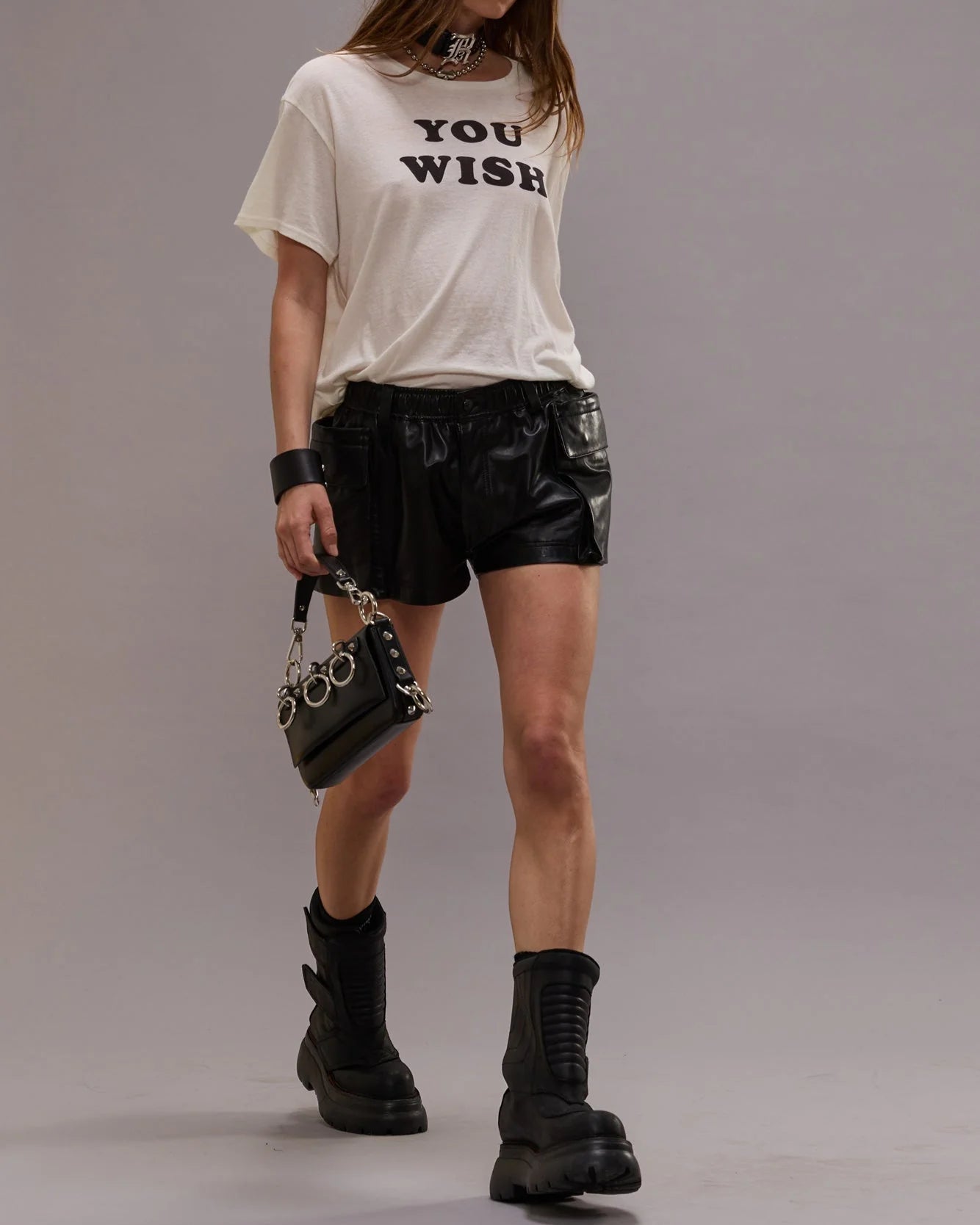 Person wearing a white t-shirt with text, black leather shorts, and black boots on a plain background