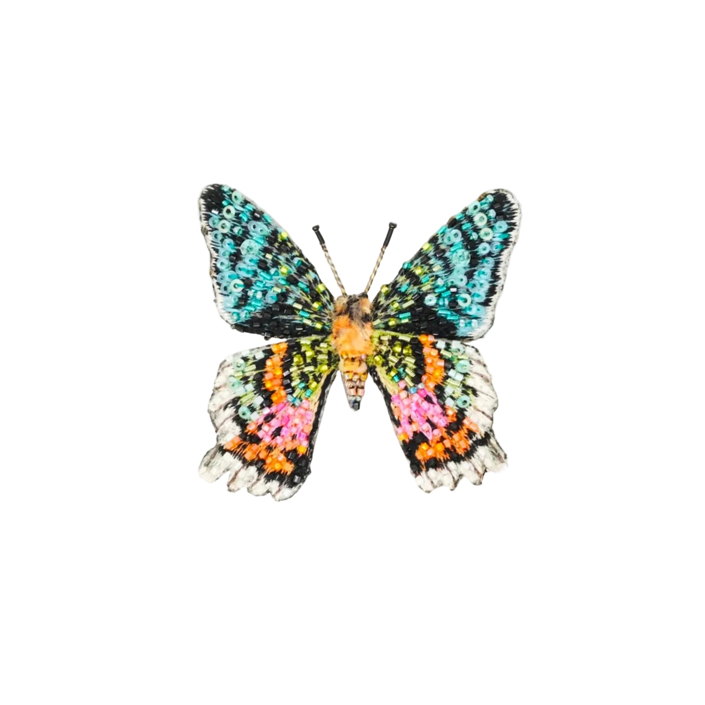 A butterfly-shaped brooch or pin with iridescent, multicolored wings in turquoise, black, orange, pink, and white, centered on a light beige background.