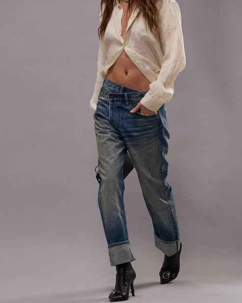Woman wearing a white blouse and blue jeans against a gray background