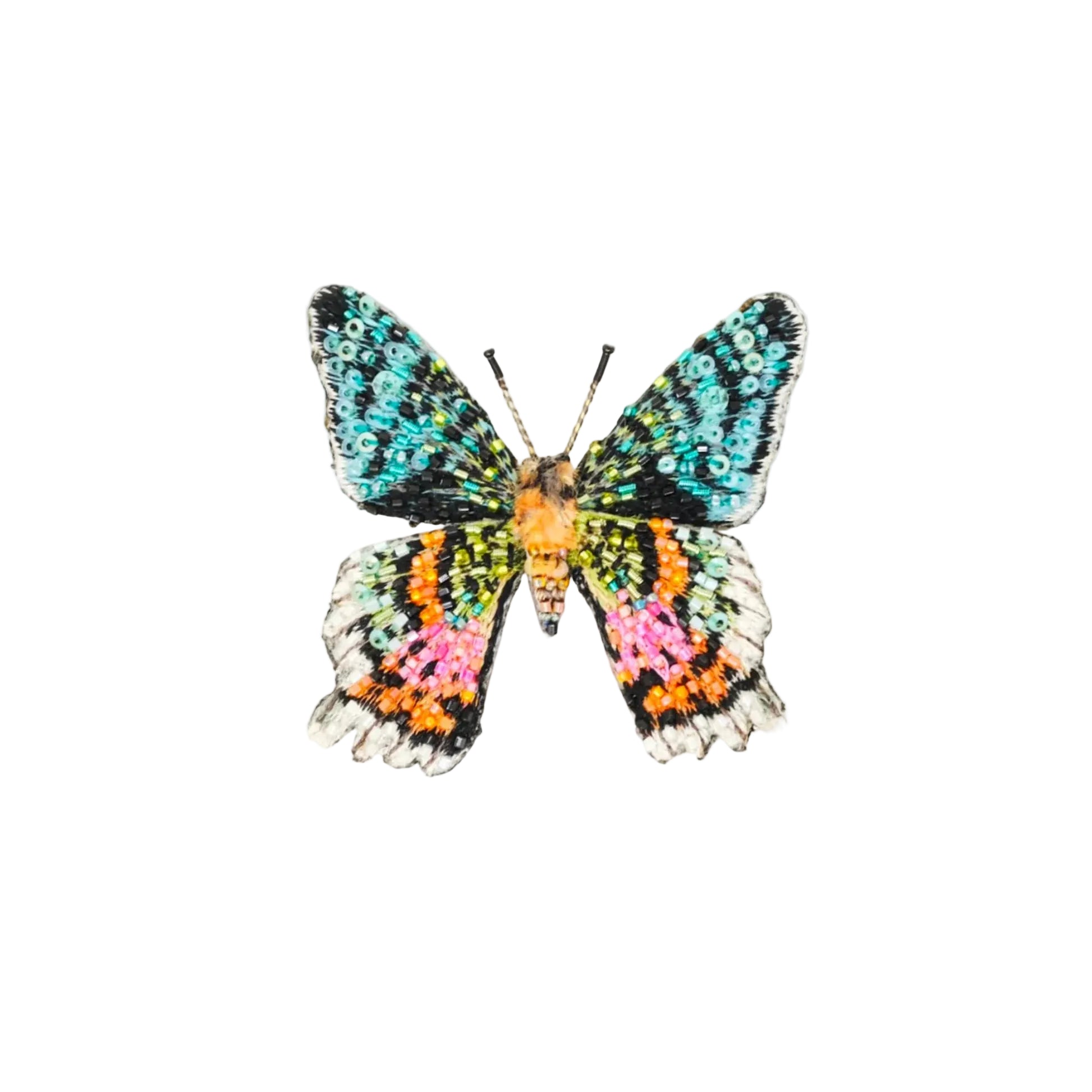 A butterfly-shaped brooch or pin with iridescent, multicolored wings in turquoise, black, orange, pink, and white, centered on a light beige background.